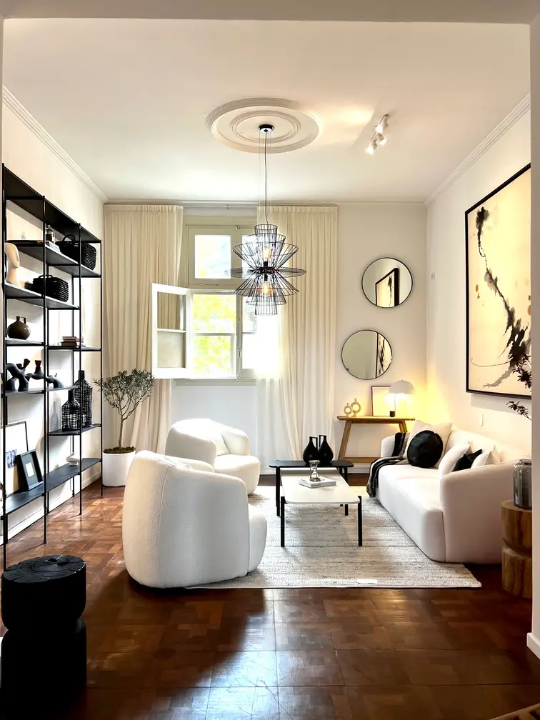 Living luminoso con sillones claros, mesa ratona y un espejo de marco dorado.