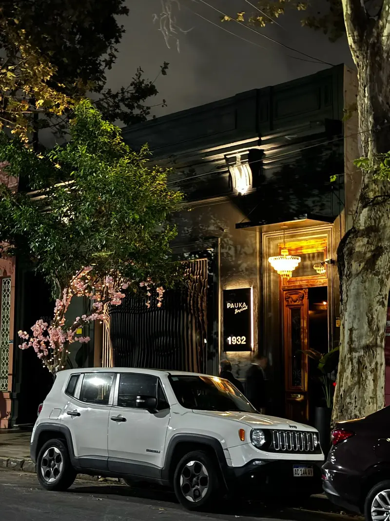 Fachada de PAUKA con vegetación, esculturas y el acceso iluminado de noche.